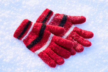 Red winter wool gloves are lying on pure white snow. texture. wallpaper. background. winter holiday concept