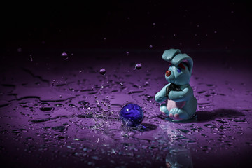 Toy rabbit with a blue ball on a purple background in the rain