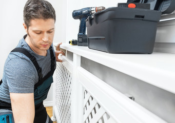 Professional handyman assembling radiator cabinet at home.