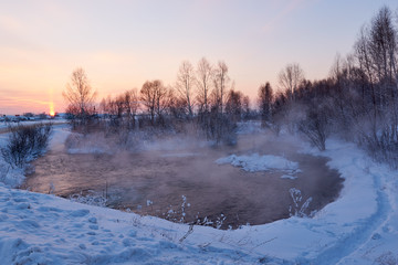 village lake in winter at sunset. fog floating over the lake. frosty evening