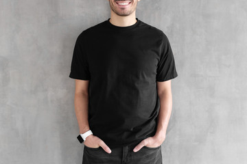 Hotizontal portrait of young man wearing blank black t-shirt and jeans, posing against gray...