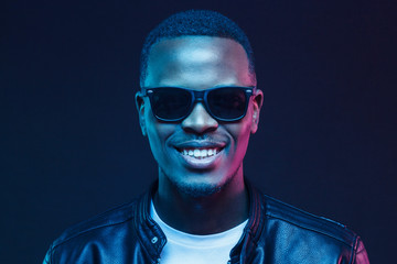 Close-up studio shot of smiling african american male model wearing trendy sunglasses and leather jacket