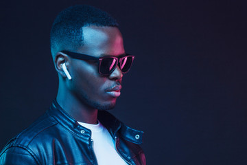 Handsome African American man wearing wireless earphones and leather jacket