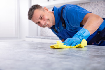 Smiling Male Janitor Cleaning Kitchen Counter