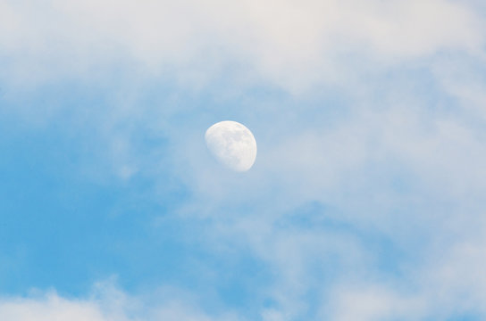 Half bright moon on blue sky background with clouds on day time