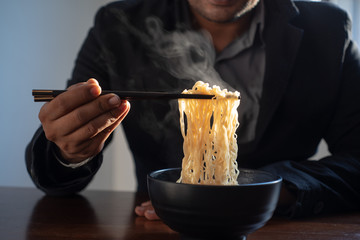 Handsome businessman hand uses chopsticks noodles with steam and smoke in bowl , selective focus....
