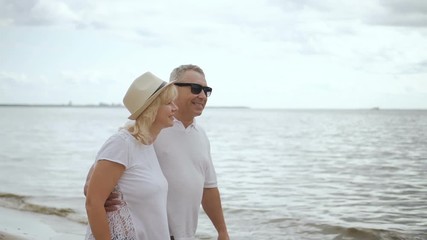 Retired man and mature woman looking to ocean surface together. Married couple standing on beach enjoying togetherness. - Powered by Adobe