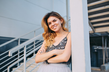 Portrait of beautiful model in grey shirt  leaning on pillar on stairs background. She is smiling to camera