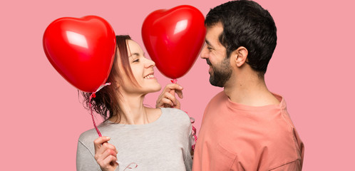 Couple in valentine day holding a heart symbol and balloons over isolated pink background