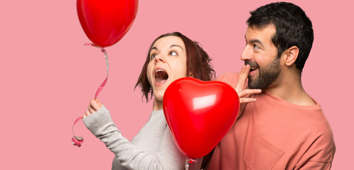 Couple in valentine day with balloons with heart shape over isolated pink background
