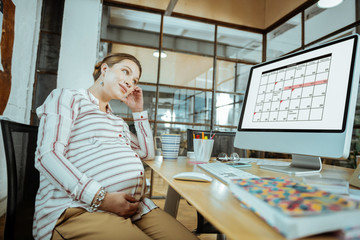 Pregnant employed mature woman sitting in front of computer