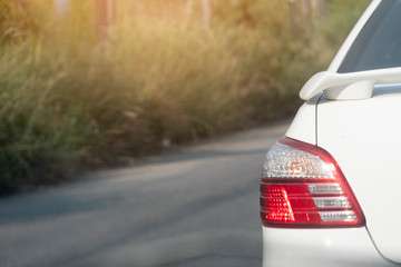 Backside of white car and break light on asphalt road with grass on beside.