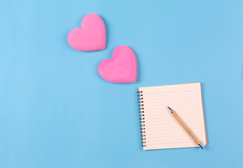 Beautiful pink hearts on pastel blue background and pen on notebook. Valentines day concept