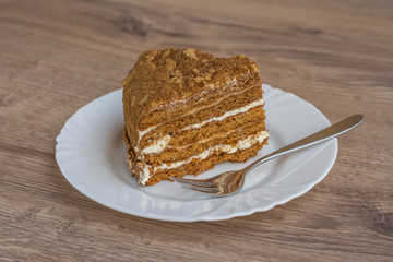 Cake on a white plate with a fork on a wooden background