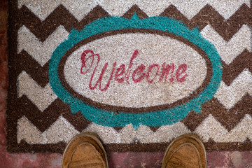 Welcome mat with feet standing next to sign