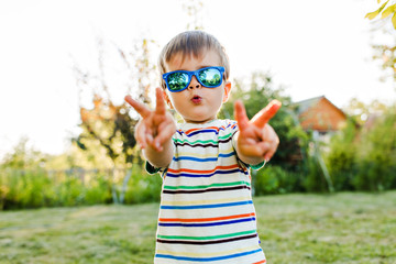 Little cute boy having fun and looks very serious in his sunglasses in the garden