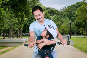 Happy father riding bicycle with his son in the park