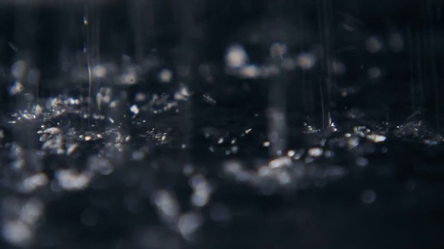 Mystic splashes of rainy water lighting a cave land with black dots in slo-mo 