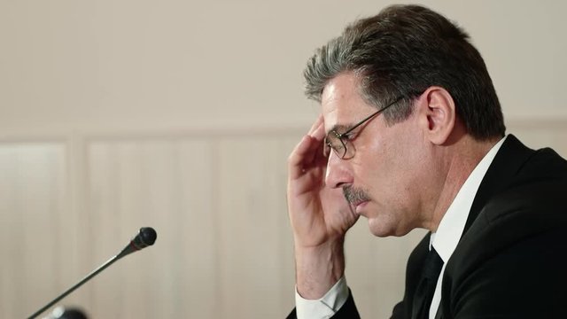 Troubled speaker attentively listens to a question from the journalist at a press conference and answers it, side view.