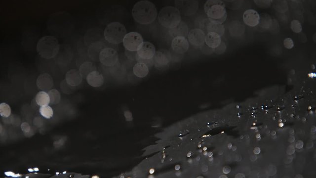 Drops of rainy water covering dark surface with spotty shadows in slow motion  