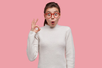 Photo of surprised Caucasian lady makes okay gesture with astonished look, agrees with something,...