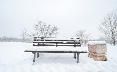 Wooden bench and concrete garbage or junk can on the street or in the park covered with snow in the winter season