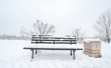 Wooden bench and concrete garbage or junk can on the street or in the park covered with snow in the winter season - Powered by Adobe