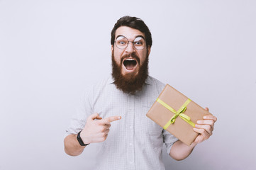 Handsome excited bearded man, holding and pointing at small gift box