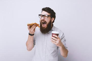 Happy hungry bearded man eating a slice of pizza and hold his cup of coffee