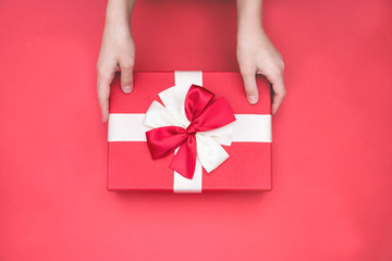 Real box with white and red bow and ribbon in hands top view on Valentine's day isolated on red background. Flat lay. Copy space