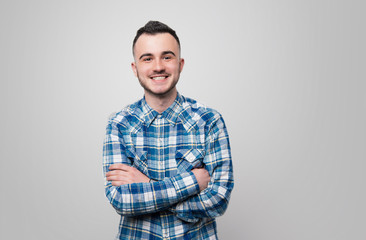 Happy young guy in blue checkered shirt, is crossing hands and looking at camera