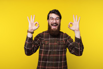 Fototapeta premium Handsome bearded man in round glasses and shirt is gesturing okay, like symbol