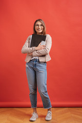 Young smiling student or intern in eyeglasses standing with a folder on red background.