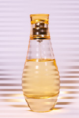 Warm yellow colour glass parfum bottle on white-purple background. Photo contains stripes.
