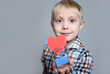 Blond little boy holding a metal shopping trolley with a heart shaped postcard inside