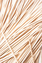 A bunch of unused round toothpicks from light-colored wood arrayed on a white plain background.