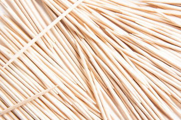 A bunch of unused round toothpicks from light-colored wood arrayed on a white plain background.