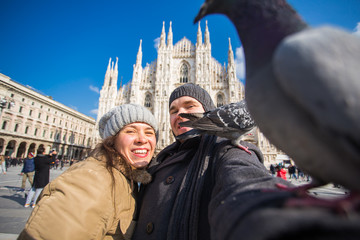 Couple taking self portrait with pigeon in Duomo square in Milan. Winter traveling, Italy and relationship concept