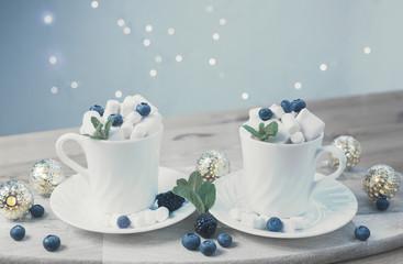 coffee with milk and marshmallows with blueberries and blackberries in white cups on wooden textured background. image