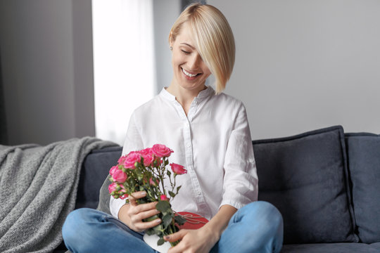 Smiling female with bouquet and gift on sofa