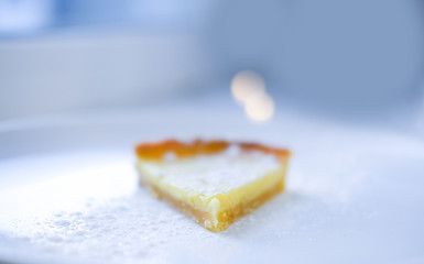 unfocused close up piece of lemon tart sprinkled with sugar powder and served on white plate