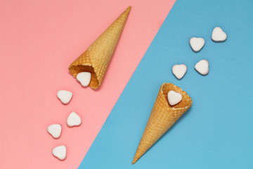Ice cream waffle cones on pastel pink and blue background, top view, flat lay. Valentine's Day. Many hearts fall out of the waffle cones.