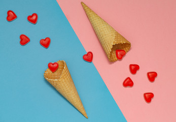Ice cream waffle cones on pastel pink and blue background, top view, flat lay. Valentine's Day. Many hearts fall out of the waffle cones.
