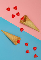 Ice cream waffle cones on pastel pink and blue background, top view, flat lay. Valentine's Day. Many hearts fall out of the waffle cones.