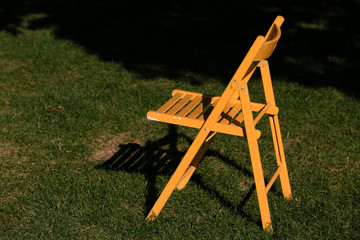 yellow folding wooden chair in the sun rays on the green grass