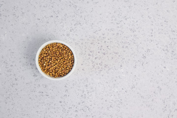 Dry buckwheat in white ceramic bowl isolated on grey table. Spilled buckwheat.