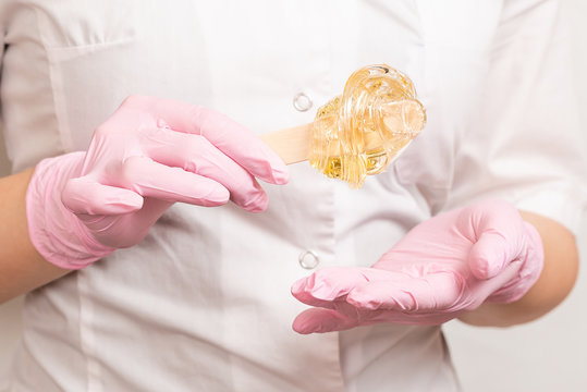 sugar paste for sugaring and depilation on a wooden stick in the hands of a beautician in pink latex gloves