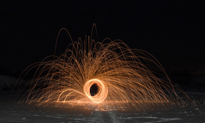 Light painting art. Spinning steel wool in abstract circle, firework showers of bright yellow glowing sparkles on winter snowy valley.