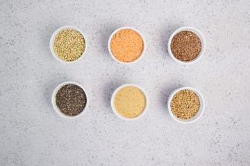 Collection of different groats on grey background. Top view of buckwheat, chia, flax, amaranth, lentils, couscous, wheat