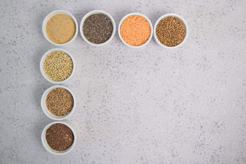Collection of different groats on grey background. Top view of buckwheat, chia, flax, amaranth, lentils, couscous, wheat